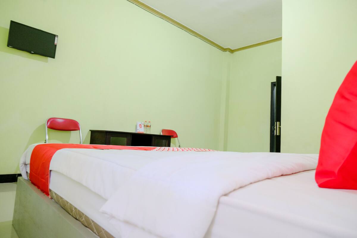 Ein Hotelzimmer mit einem Bett, zwei roten Sessel, einem Schreibtisch und einem Fernseher an der Wand.