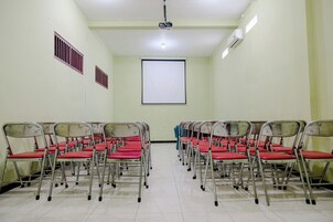 Un salón de conferencias con filas de sillas plegables, una pantalla de proyector y rejillas de ventilación en las paredes.
