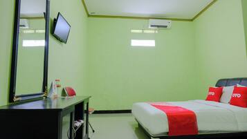 A hotel room with a bed, a desk with a mirror, a television, and an air conditioning unit.