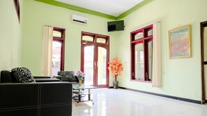 A spacious lobby with a black sofa, a small table with a vase of flowers, and a large window with red frames. - Oyo 2508 Alba Suites Homestay (Tulungagung)