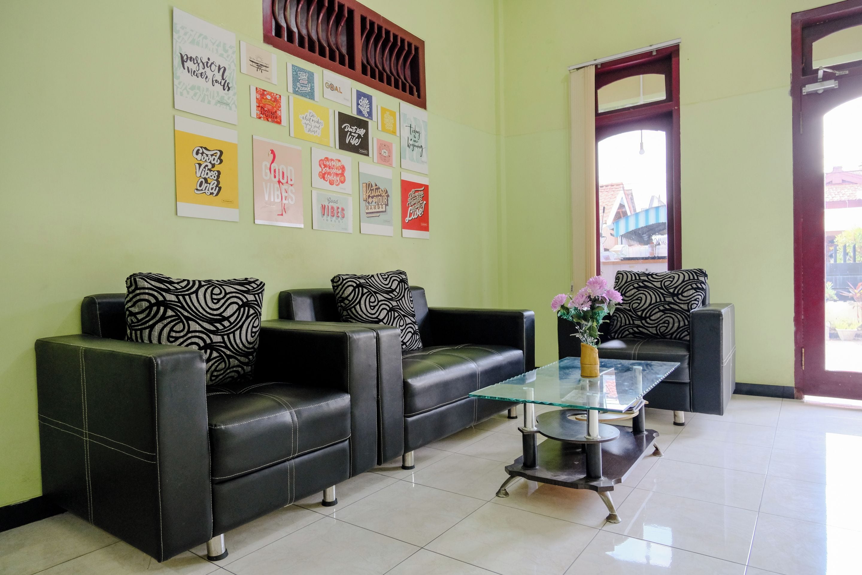 Un área de recepción con tres sofás de cuero negro, una mesa de centro de vidrio y una pared decorada con carteles motivacionales.