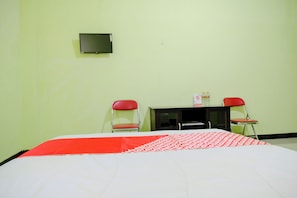 A room with a bed, two red chairs, a small table, and a wall-mounted TV.