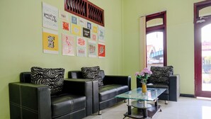 A reception area with three black leather sofas, a glass coffee table, and motivational posters on the wall. - Oyo 2508 Alba Suites Homestay (Tulungagung)