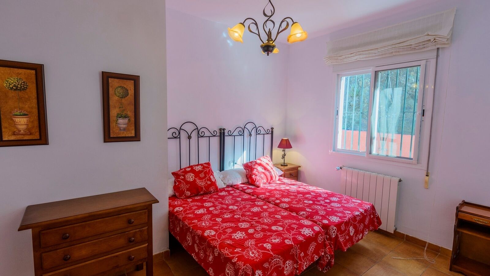 A bedroom with a bed, dresser, nightstand, lamp, window, and two framed pictures on the wall.