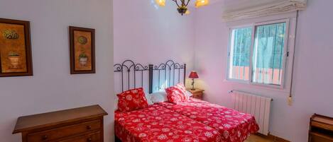 A bedroom with a bed, dresser, nightstand, lamp, window, and two framed pictures on the wall.