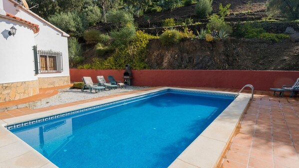 A rectangular swimming pool with a tiled edge, surrounded by a red wall and a stone pathway. - Villa Lantana Algarrobo by Ruralidays (Málaga)