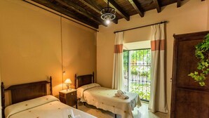Una stanza con due letti, un comodino con lampada, una finestra con tende e un armadio in legno.