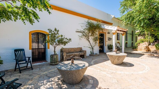 Patio esterno con pavimento in pietra, una sedia nera, un tavolo in pietra e una piccola fontana.