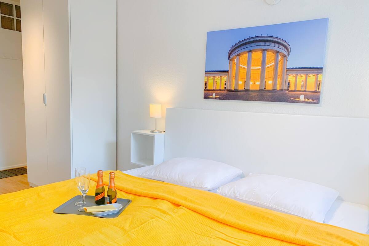 Quarto de hotel com uma cama, mesa de cabeceira, luminária e pintura de um edifício.