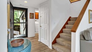 A hallway with a wooden staircase, a white door, and a glass door leading outside.