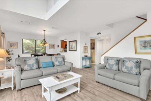 A spacious living room with a grey sofa set, a white coffee table, and a staircase leading to another level.