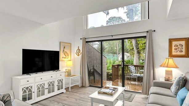 A living room with a TV, white cabinet, sofa, and a sliding glass door leading to a patio.
