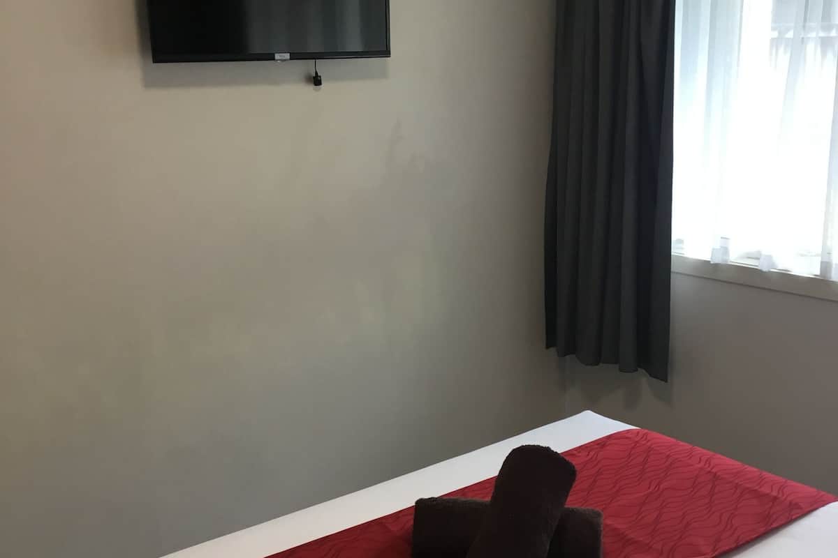 Ein Hotelzimmer mit einem Bett, einem flachbildfernseher an der Wand und einem fenster mit Vorhängen.