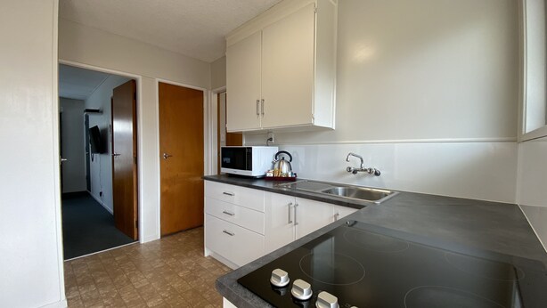 A kitchen with white cabinets, a black stovetop, and a microwave. - Ulster Apartments (Hamilton)