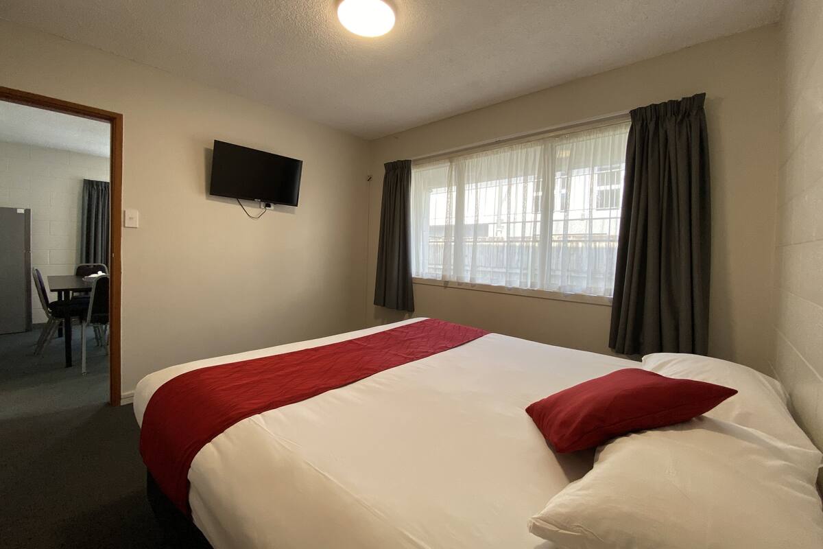 Ein Hotelzimmer mit Bett, Wandfernseher und einem fenster mit Vorhängen.