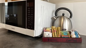 A Panasonic microwave oven with a digital display and control panel, a stainless steel kettle, and a box of assorted food items including chocolate, biscuits, and bread. - Ulster Apartments (Hamilton)