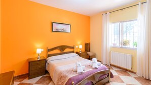 A hotel room with a bed, two bedside tables, a nightstand, a window with curtains, and a picture on the wall.