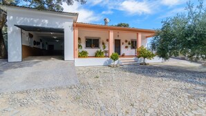 A two-story house with a covered garage, a front porch with potted plants, and a gravel driveway.