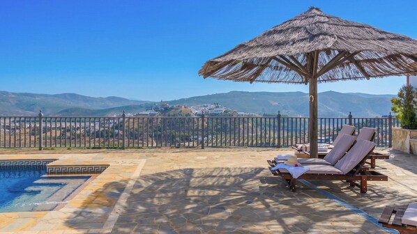A pool area with lounge chairs and a thatched umbrella, overlooking a mountainous landscape. - El Mirador de Iznájar by Ruralidays (Córdoba)