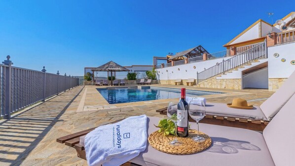 A poolside area with a lounge chair, a bottle of wine, and a towel with branding. - El Mirador de Iznájar by Ruralidays (Córdoba)