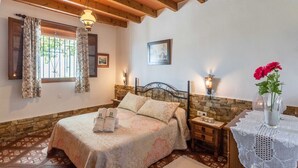 Un dormitorio acogedor con cama, mesita de noche, un jarrón con flores y ventana con cortinas.