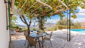 Un patio techado con mesa y sillas, una piscina y vistas a las montañas.