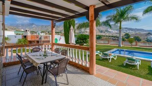 A covered patio with a table and chairs, a pool, and a view of the mountains. - Villa Pastora Nerja by Ruralidays (Málaga)