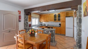 A kitchen with wooden cabinets, a stone accent wall, a dining table with chairs, and a fruit bowl. - Villa Pastora Nerja by Ruralidays (Málaga)