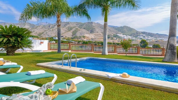 A pool area with lounge chairs, a swimming pool, and a view of a mountainous landscape. - Villa Pastora Nerja by Ruralidays (Málaga)