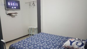 Una camera da letto con un letto, una TV a muro, un piccolo tavolino e una sedia.