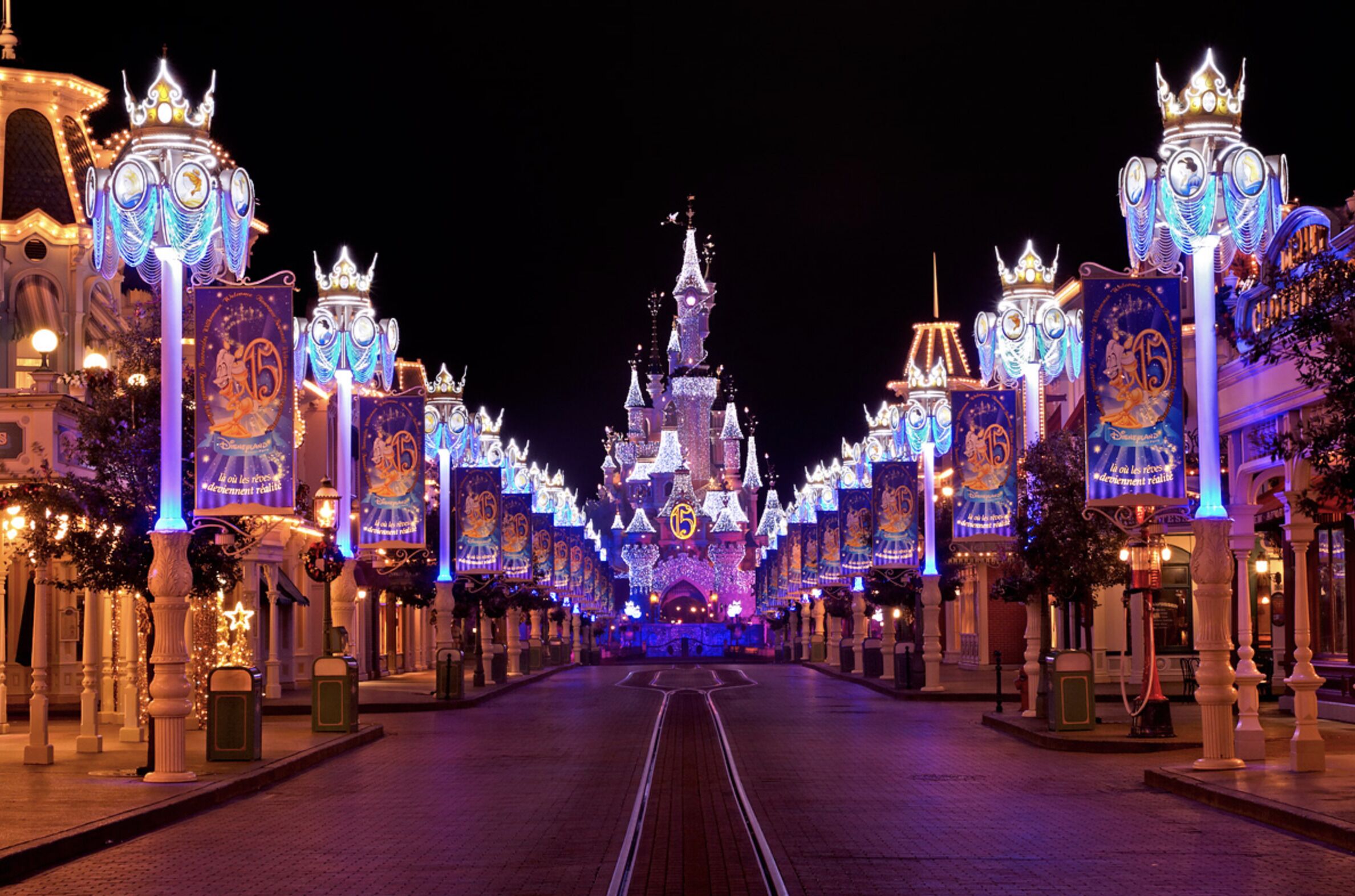 Un imposant bâtiment illuminé, surmonté d’une flèche centrale et flanqué de colonnes et de bannières, créant une atmosphère symétrique et festive.