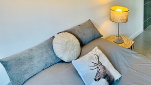Un lit avec une literie grise, une lampe et un coussin orné d’un motif de cerf.