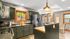 Une cuisine moderne avec des meubles de couleur sombre, un réfrigérateur en acier inoxydable et un îlot central en bois.