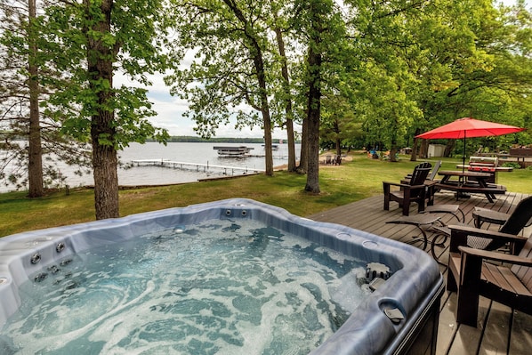Un bain à remous sur une terrasse avec vue sur le lac, entouré d’arbres et de mobilier d’extérieur.