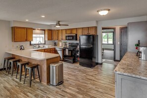 Una cocina moderna con armarios de madera, un refrigerador de acero inoxidable y una barra con taburetes.