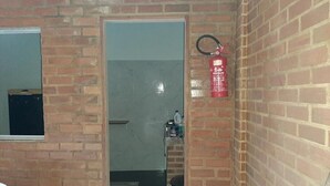 A room with a brick wall, a fire extinguisher mounted on it, a door leading to another room, and a window with a view of the outside.