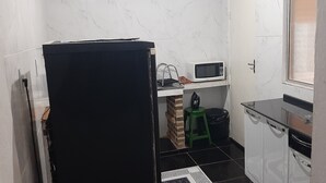 A compact kitchen with a refrigerator, microwave, sink, and a small stool.