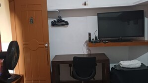 Una habitación compacta con una cama, un escritorio con una computadora, un televisor y un reloj de pared.