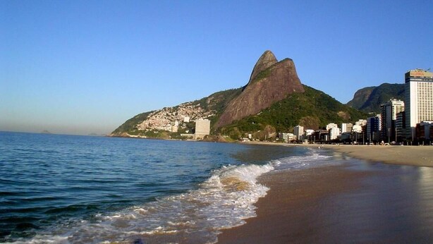 A beach with a prominent mountain in the background and a cityscape with buildings along the shore.