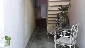 A narrow corridor with a small seating area featuring a glass table and metal chairs, a potted plant, and a door at the end.