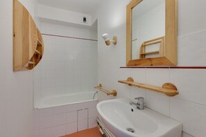 A bathroom with a bathtub, a sink, a mirror, and wooden shelves.