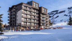 A multi-story hotel with balconies, a ski slope in the background, and outdoor seating.
