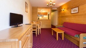 Ein gemütliches Zimmer mit Holzwand, einem Fernseher, einem Esstisch mit Stühlen, einem roten Sofa und einem violetten Teppich.