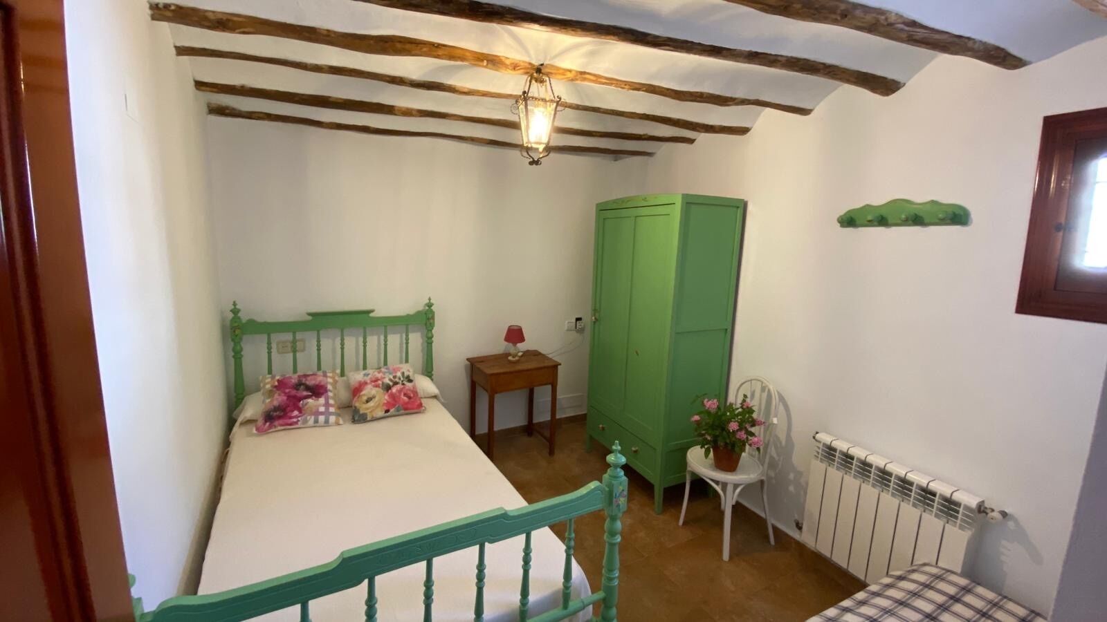 Un dormitorio con una cama, un armario verde, una mesita con lámpara y un radiador.