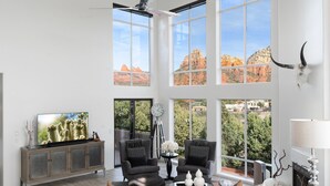 A spacious living room with large windows, a flat-screen TV, two armchairs, a sofa, and a fireplace. - FEATURED in FORBES, 20ft ceilings, AMAZING views, + loft, hot tub, fire pit, EV. (Sedona)