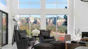 A modern living room with a large window offering a view of red rock formations. - FEATURED in FORBES, 20ft ceilings, AMAZING views, + loft, hot tub, fire pit, EV. (Sedona)