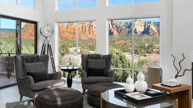 A modern living room with two grey armchairs, a round coffee table, and a large window overlooking a scenic canyon view. - FEATURED in FORBES, 20ft ceilings, AMAZING views, + loft, hot tub, fire pit, EV. (Sedona)