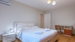 Un dormitorio con cama, mesita de noche, escritorio, silla y equipo de aire acondicionado.