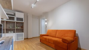 Una sala de estar moderna con piso de madera, un sofá naranja brillante y estanterías empotradas con diversos objetos.
