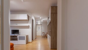 Un pasillo estrecho con suelo de madera, paredes blancas y una puerta al final.
